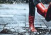 Feet of little girl wearing rubber boots stepping on small puddle