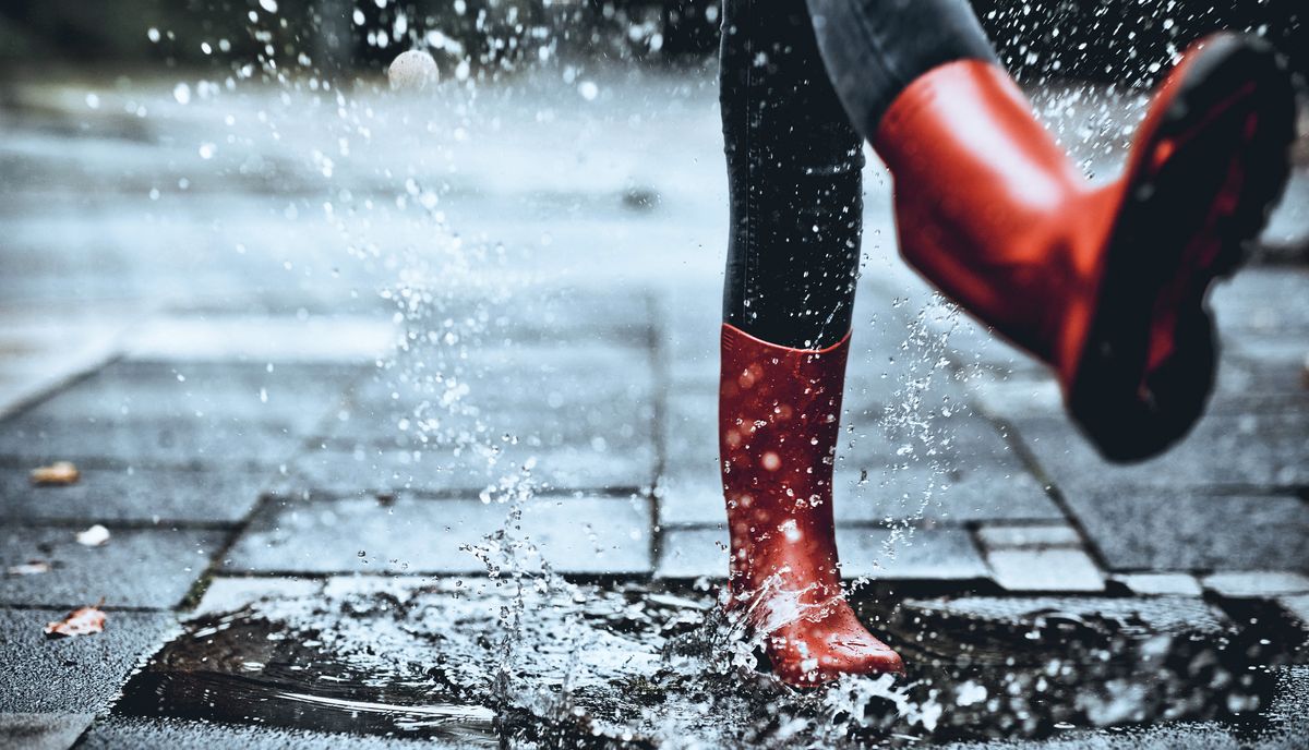 Feet of little girl wearing rubber boots stepping on small puddle